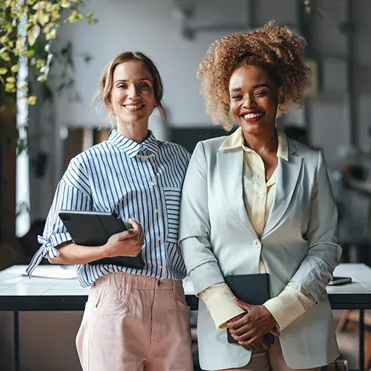 diverse-businesswomen-smiling-with-devices-in-office
